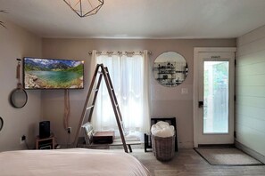 Een slaapkamer met een bed, een televisie, een ladder, een spiegel, een mand en een deur met een 'Niet roken'-bord.