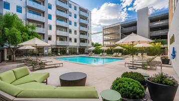 A modern hotel courtyard with a swimming pool, outdoor seating, and a multi-story building.