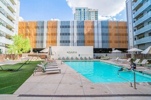 A modern hotel with a swimming pool, outdoor lounge chairs, and a view of the city skyline.