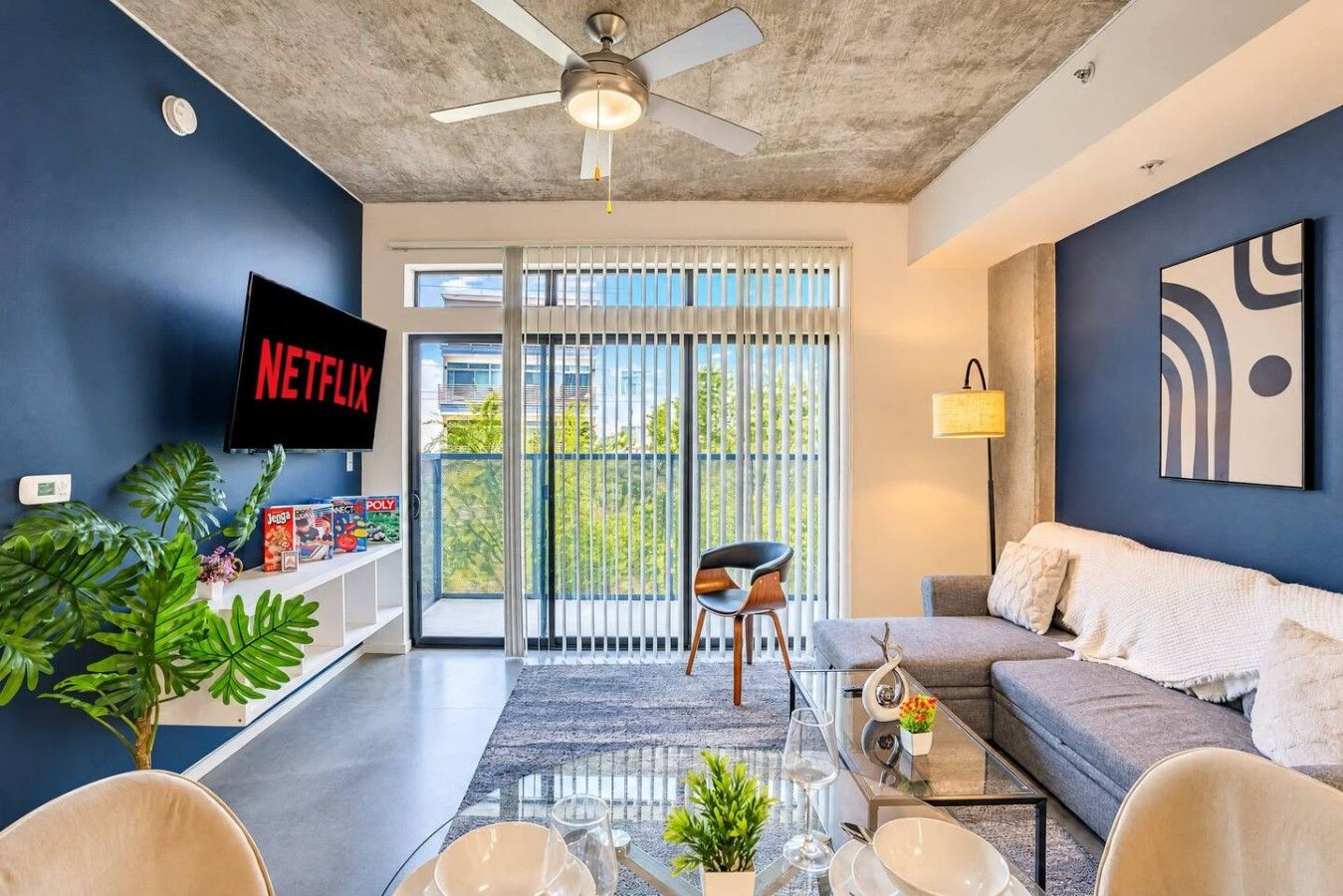 A modern living room with a flat-screen TV, a ceiling fan, a sofa, a coffee table, and a bookshelf.