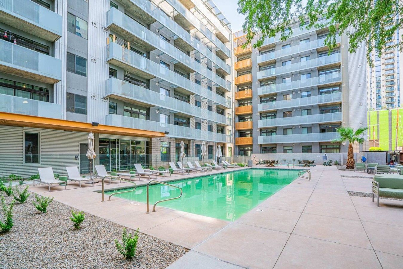 Um edifício de apartamentos moderno com piscina no terraço, área de estar externa e espaço coberto com guarda-sóis.