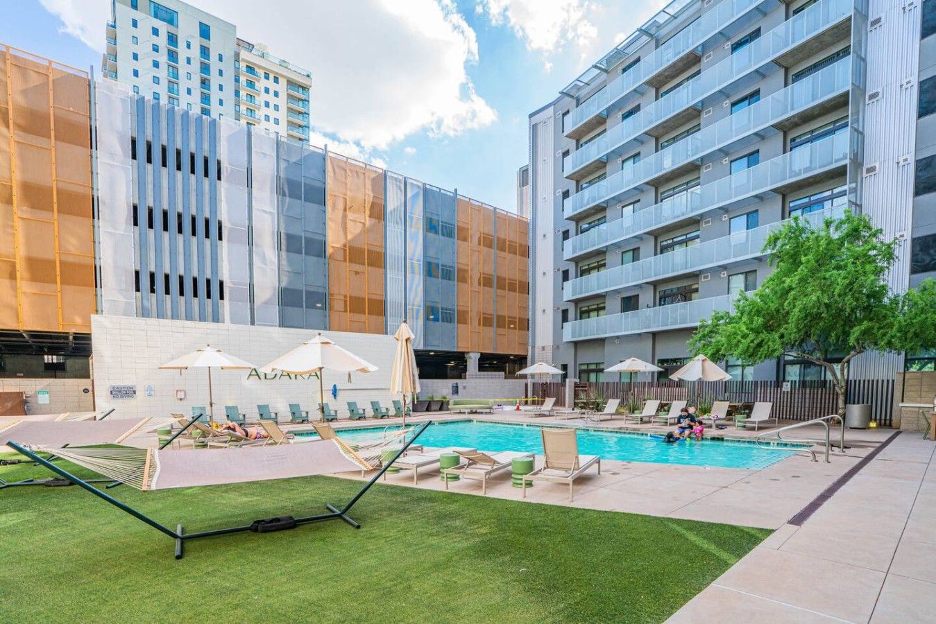 Ein modernes Hotel mit Schwimmbad, Sitzgelegenheiten im Freien und Blick auf die Skyline der Stadt.
