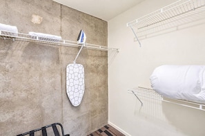 Ett hotellrum med en vägg av betong, ett hängstativ för tvätt, en strykjärnsbräda i metall och en säng med ett vitt överkast.