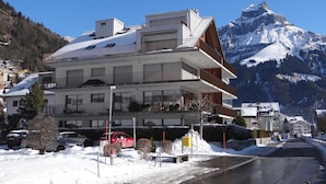 A multi-story hotel with balconies, a parking area, and a mountain backdrop.