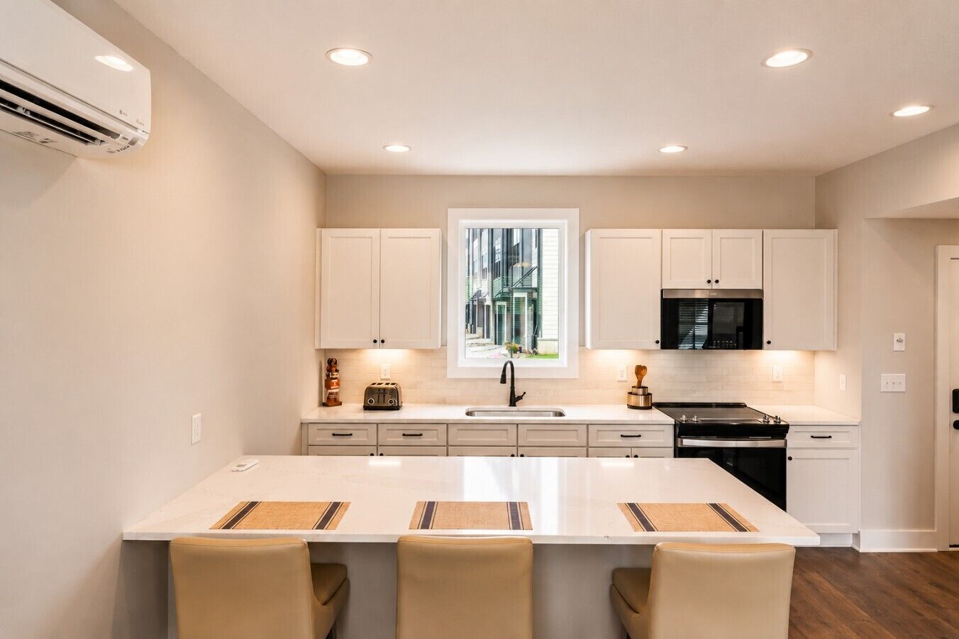 A modern kitchen with a central island, white cabinetry, and a view of a building outside.