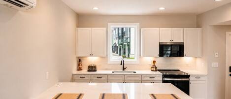 A modern kitchen with a central island, white cabinetry, and a view of a building outside.