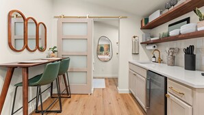 A modern kitchen with wooden cabinets, a white countertop, and a dining area with green chairs. - Romantic Hideaway | Hot Tub Near Thunder Ridge (Omaha)