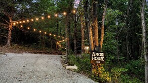 A gravel path leading to a wooden sign for Mori House, surrounded by trees and string lights. - Romantic Hideaway | Hot Tub Near Thunder Ridge (Omaha)