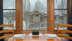 Une table à manger avec deux chaises, une petite plante et une fenêtre donnant sur un paysage enneigé.