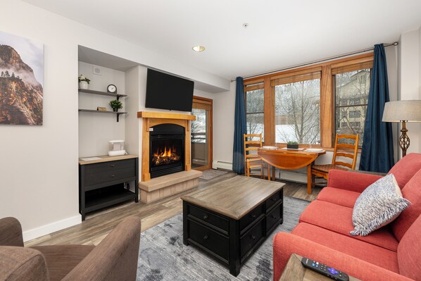 Una sala de estar con chimenea, un sofá, una mesa de centro y un televisor montado en la pared.