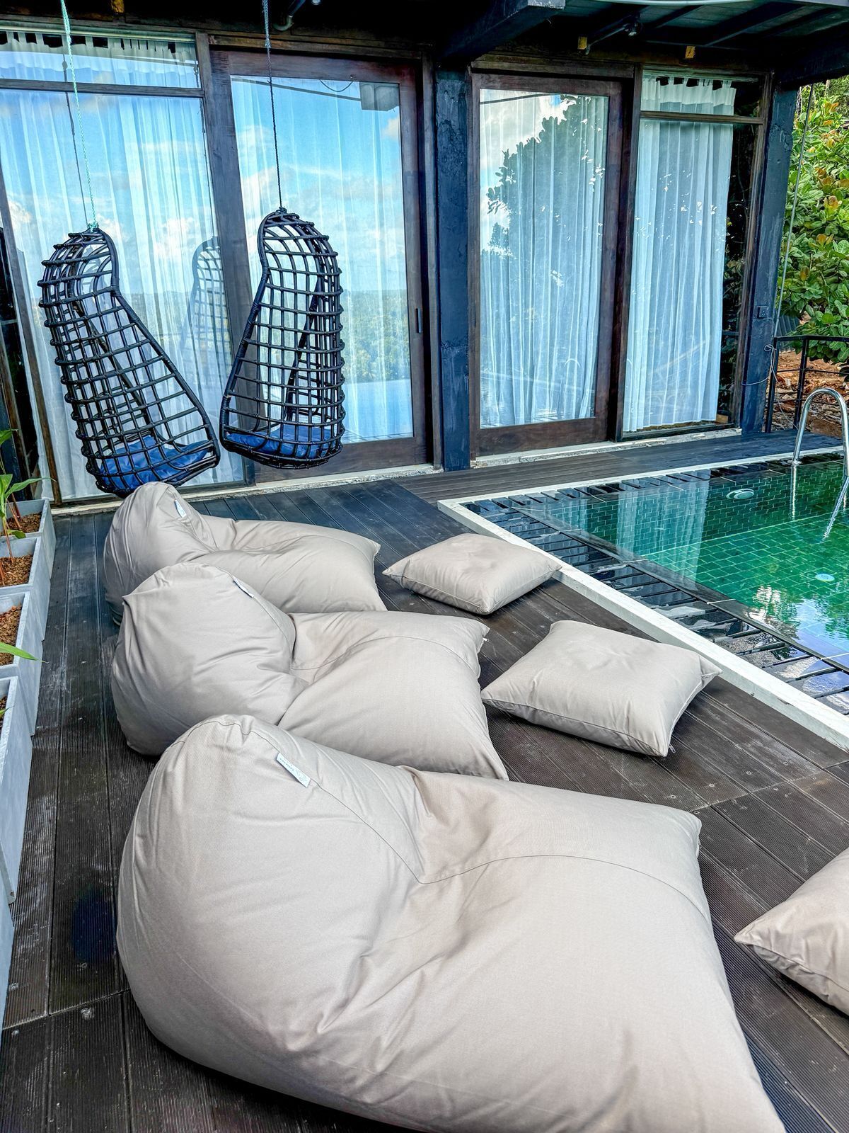 Un espace aménagé au bord de la piscine, avec des coussins de couleur beige et une piscine entourée de parois en verre.