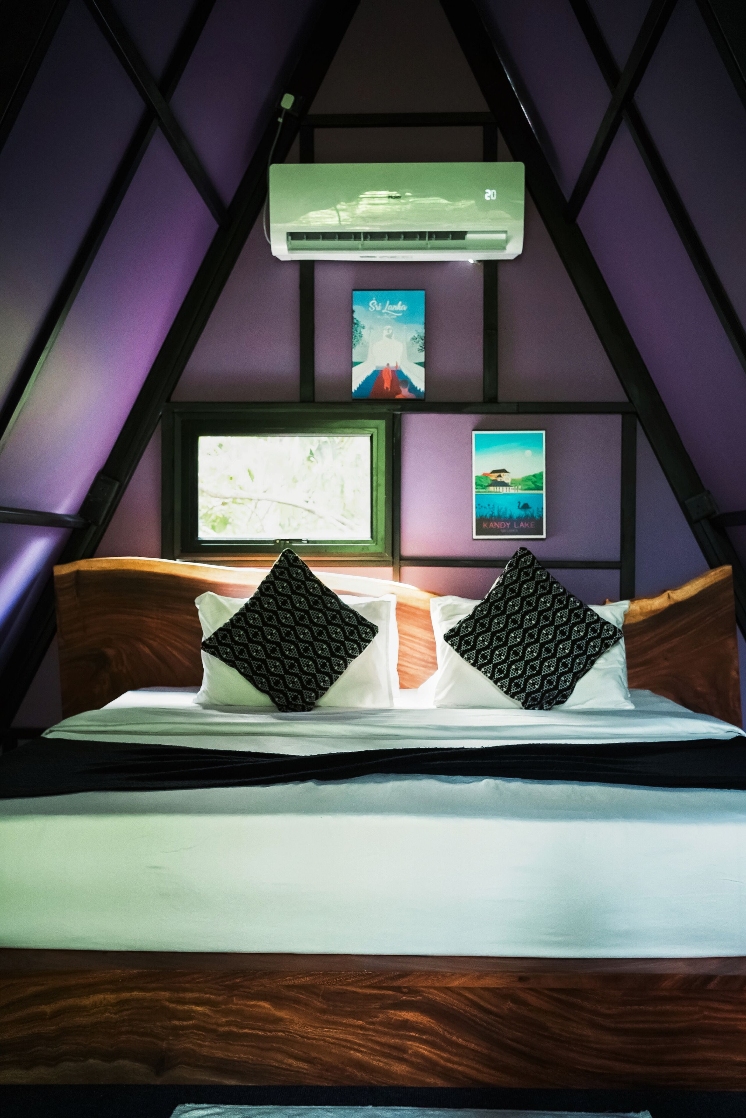 A bedroom with a bed, pillows, an air conditioner, and framed pictures on the wall.