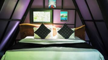 A bed with a wooden headboard, two patterned pillows, and a white bedsheet in a room with a sloped ceiling and purple walls.