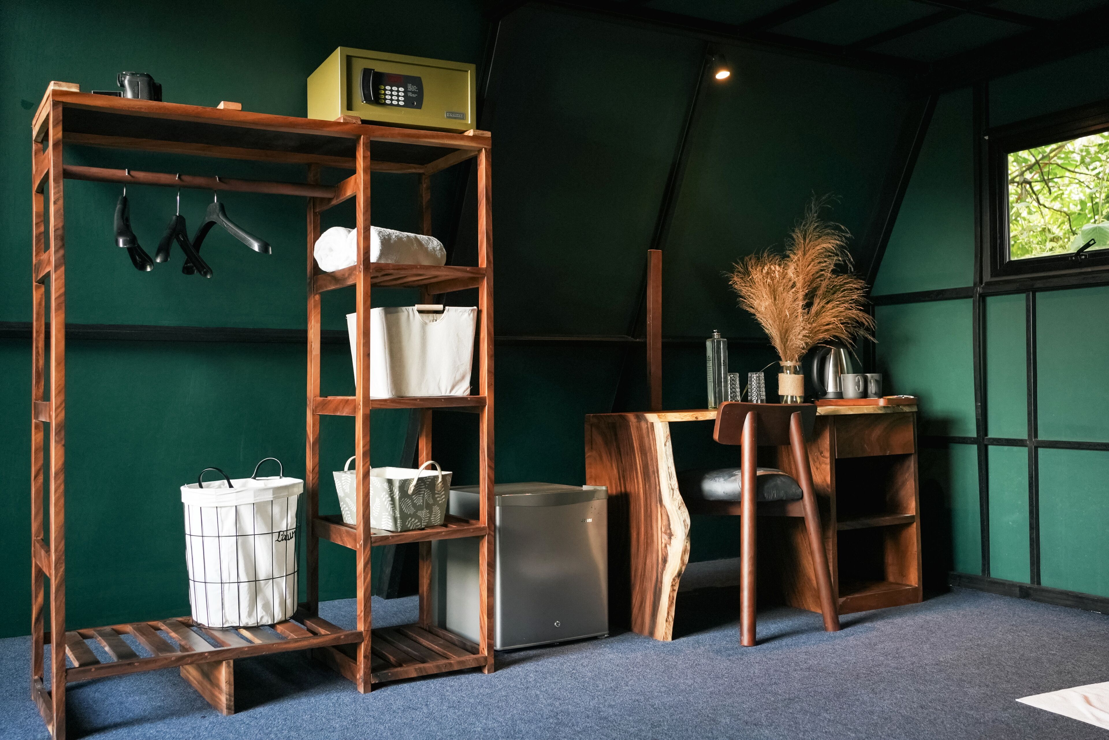 A room with a wooden shelf unit, a small refrigerator, and a window with a view of greenery.