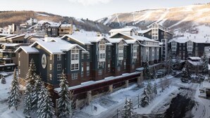 Un hôtel enneigé, composé d’un bâtiment central et de plusieurs ailes, entouré d’arbres couverts de neige et adossé à un paysage montagneux.