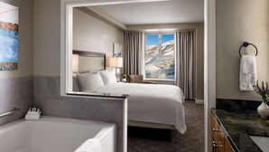 Une chambre d’hôtel avec un lit, une salle de bain avec une baignoire, un bureau et une vue sur les montagnes par la fenêtre.