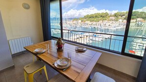 A balcony with a wooden table set for two, a view of a marina with boats, and a cityscape in the background. - 2-Bedroom Apartment with Sea View – Everything Within Walking Distance (ST MANDRIER SUR MER)