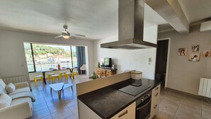 A modern kitchen with a central island, a dining area with yellow chairs, and a sofa. - 2-Bedroom Apartment with Sea View – Everything Within Walking Distance (ST MANDRIER SUR MER)