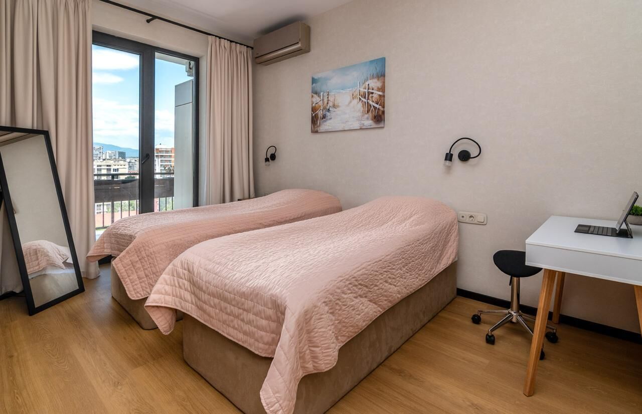 A room with two beds, a desk, a chair, a painting, and a window with curtains.