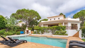 Una piscina con sillones de descanso, una barbacoa y una casa blanca con techo de tejas.