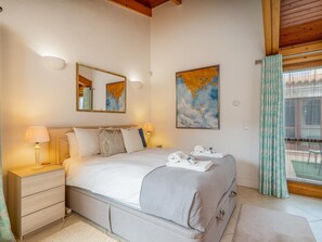 Un dormitorio con cama, mesitas de noche, una obra de arte con un mapa y una ventana con cortinas.