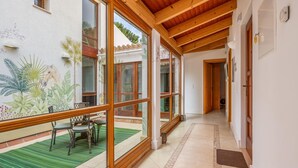 Un pasillo amplio con ventanas grandes, vigas de madera y piso de baldosas.