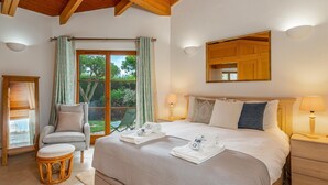 Un dormitorio bien iluminado con una cama grande, lámparas de noche, techo de madera y vistas al exterior a través de una puerta corrediza de vidrio.