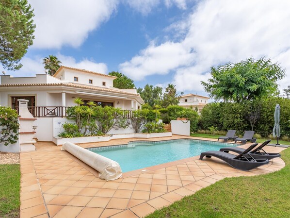 Un área de piscina con cubierta de baldosas, sillas de descanso y una pérgola cubierta.