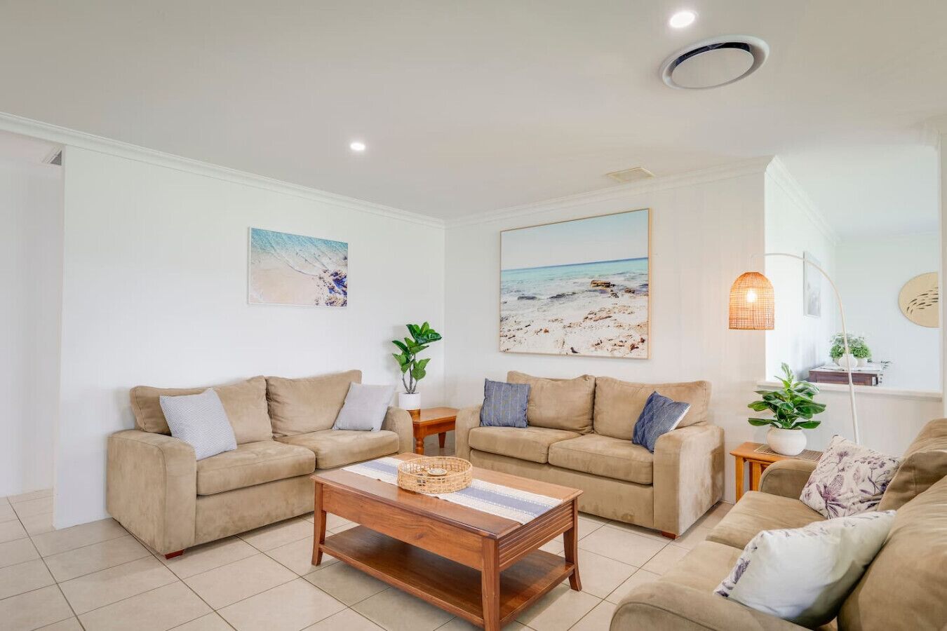 A living room with two beige sofas, a wooden coffee table, and a large beach-themed painting on the wall.
