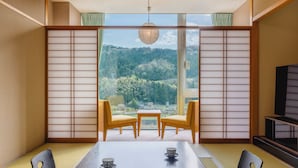A traditional Japanese room with tatami flooring, a low table with two chairs, and a view of a forested hill. - Jinzukyo Kasuga Onsen Tominowa (Toyama)