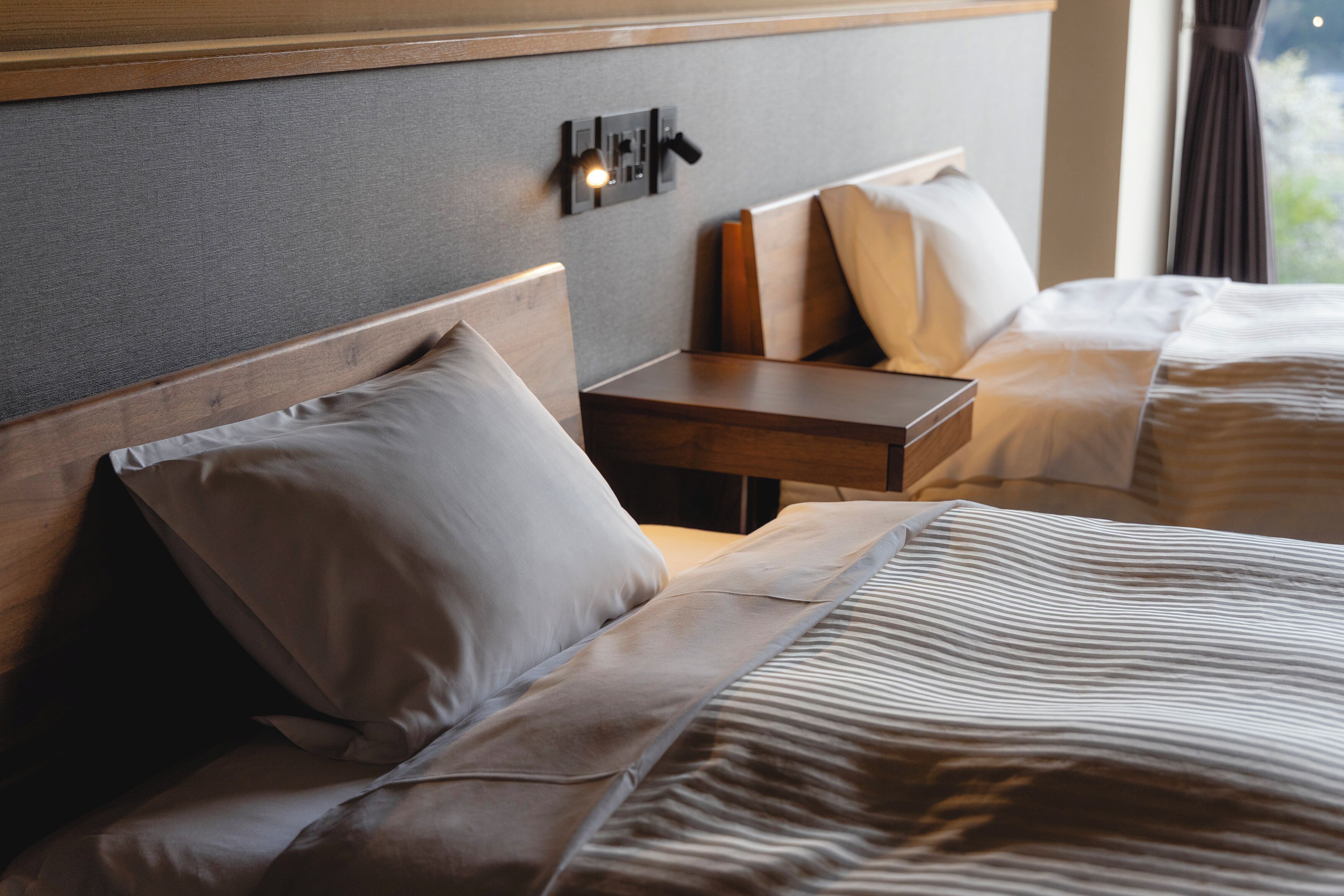 A hotel room with two beds, a nightstand, and a wall-mounted light fixture.