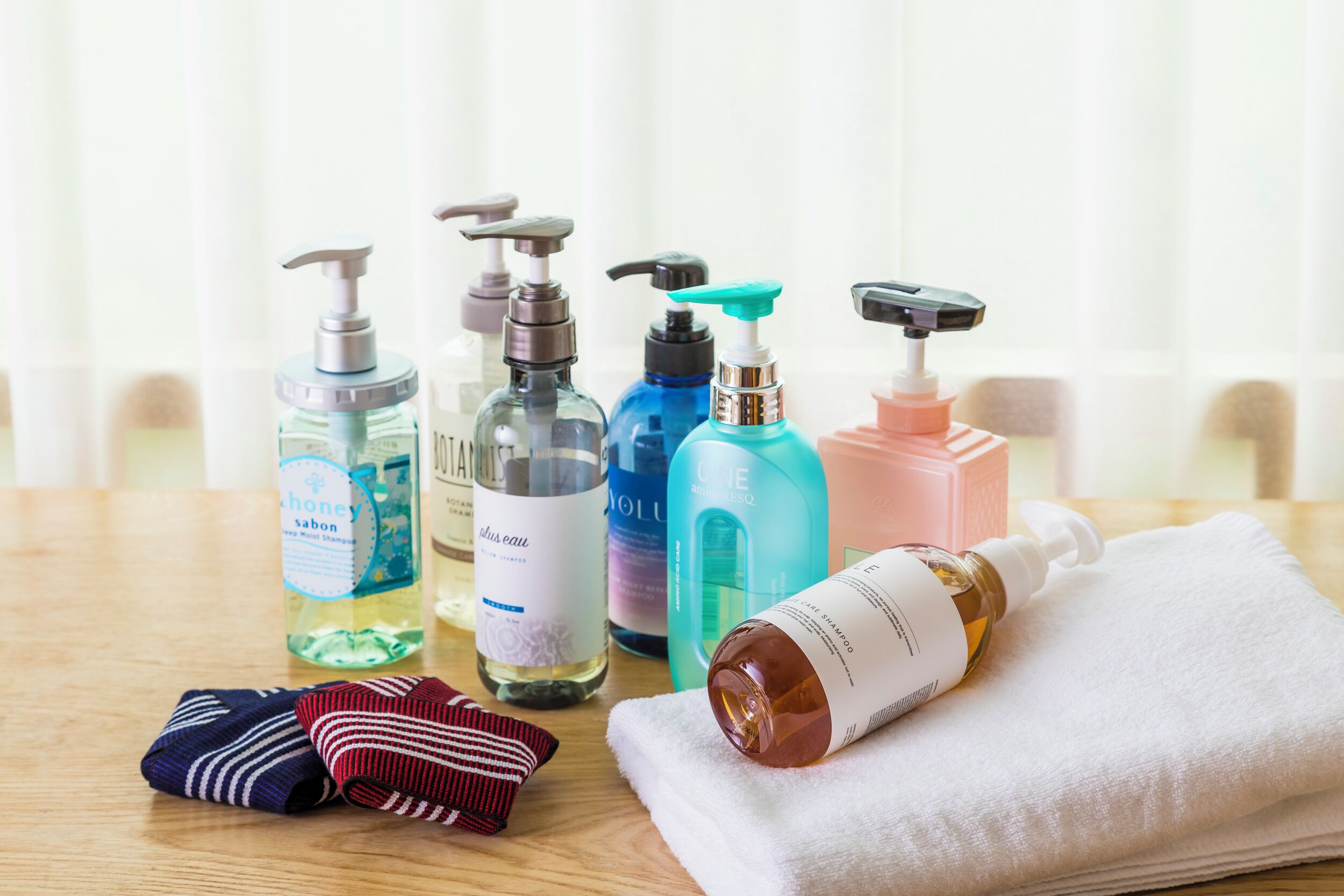 A variety of toiletries on a table, including bottles of shampoo and conditioner, a bottle of lotion, and a folded towel.