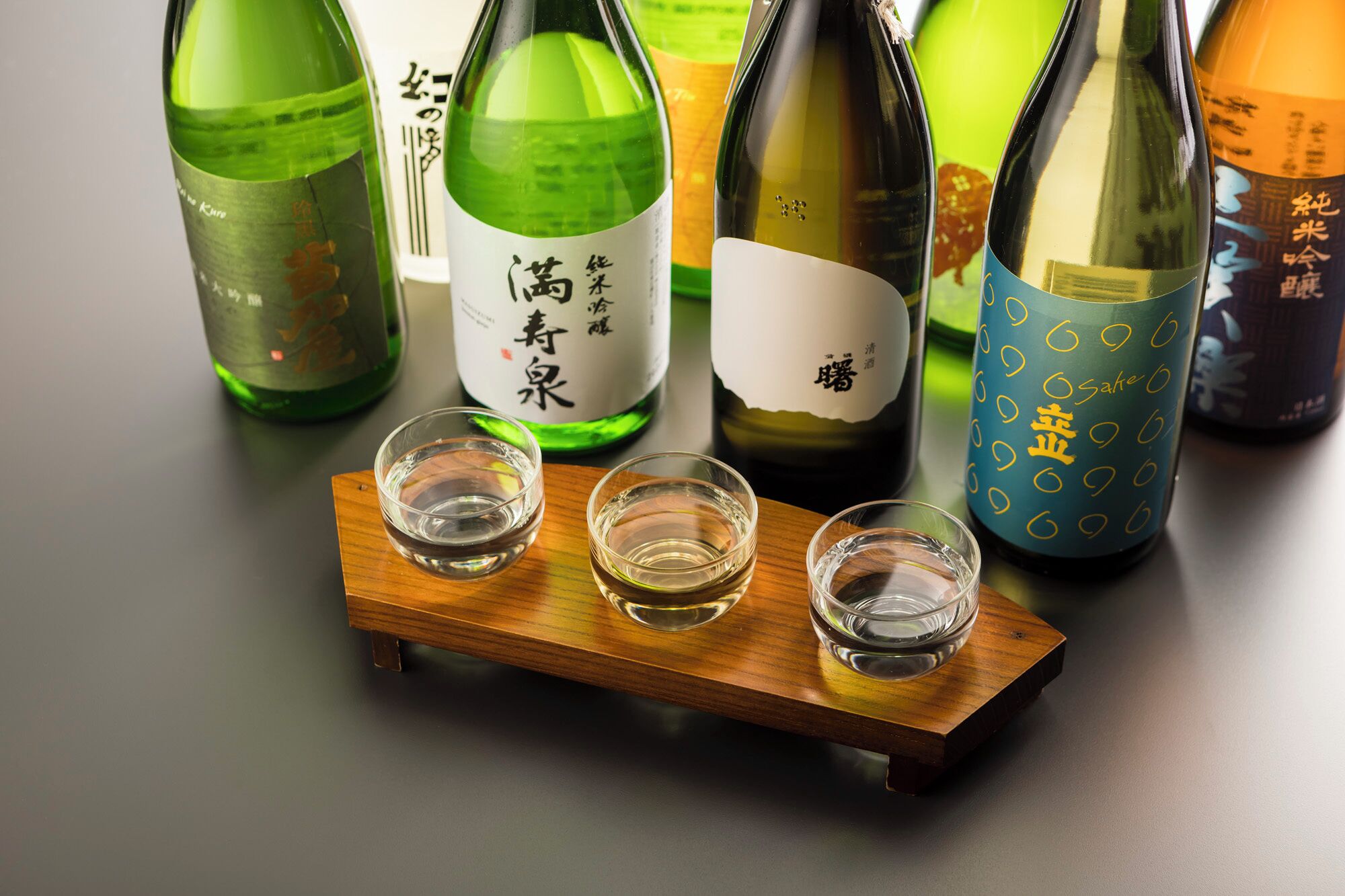Cuatro botellas de sake y tres vasos para chupitos sobre una bandeja de madera.