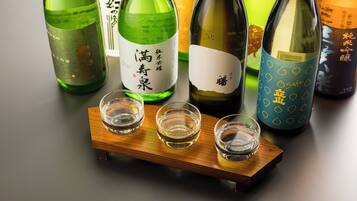 Cuatro botellas de sake y tres vasos para chupitos sobre una bandeja de madera.