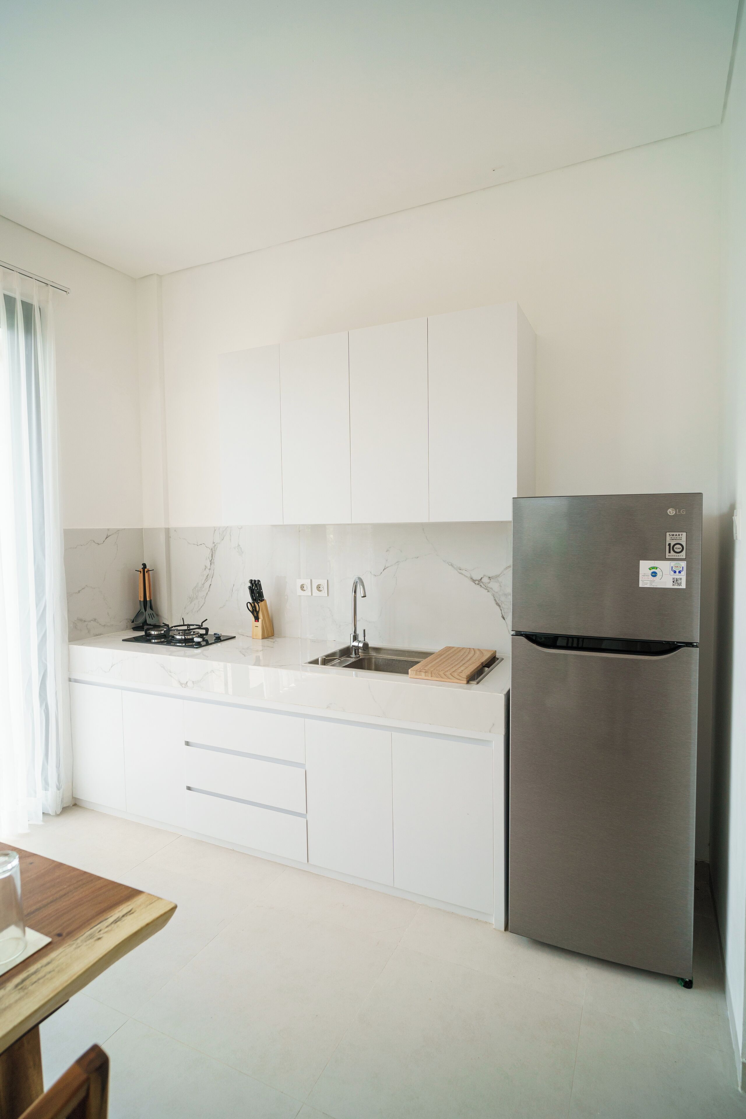 A modern kitchen with white cabinets, a stainless steel refrigerator, and a marble backsplash.