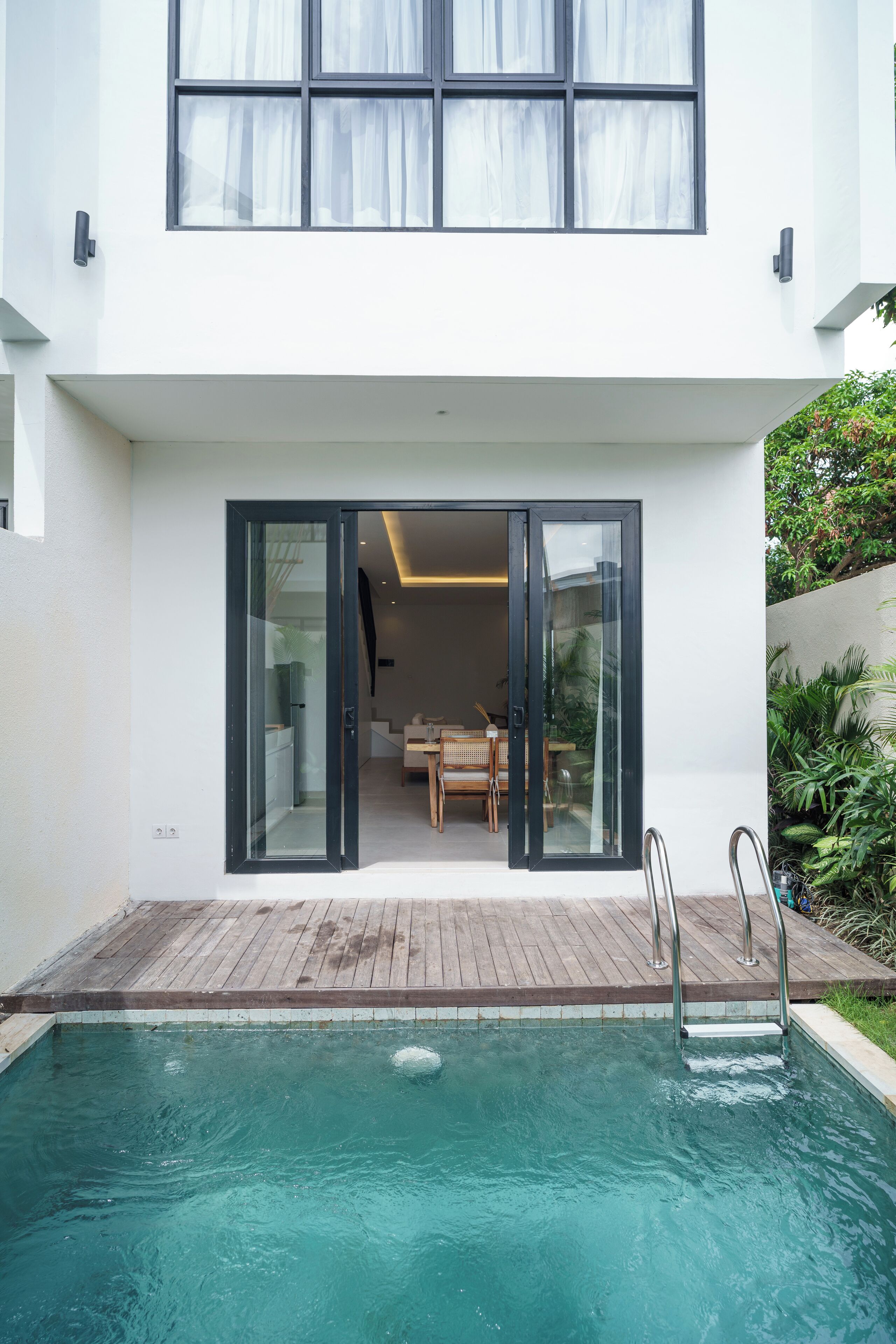 Une maison moderne dotée d’une piscine, d’un coin repas et d’une grande porte-fenêtre coulissante donnant sur l’intérieur.