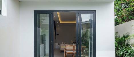 A modern house with a swimming pool, a dining area, and a large sliding glass door leading to the interior.