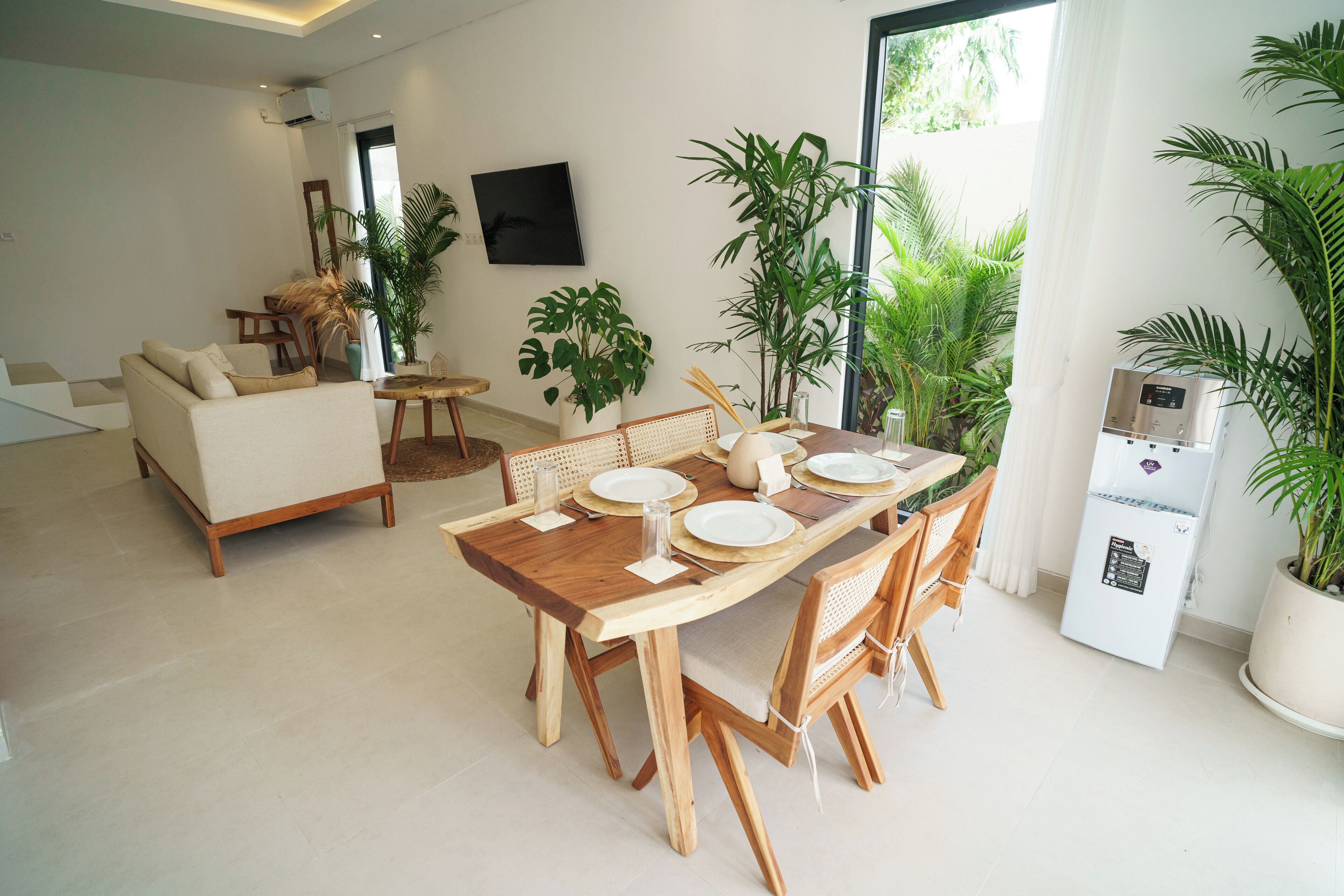 A modern living room with a wooden dining table set for four, a sofa, and a large potted plant.
