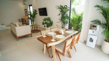 A modern living room with a wooden dining table set for four, a sofa, and a large potted plant.