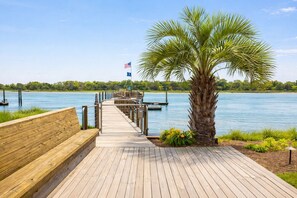 A wooden boardwalk leading to a dock with a palm tree and a flag.