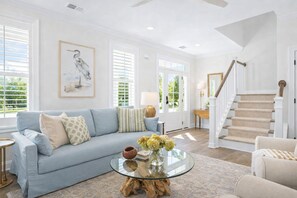 A living room with a light blue sofa, a glass coffee table, and a staircase with a wooden railing.