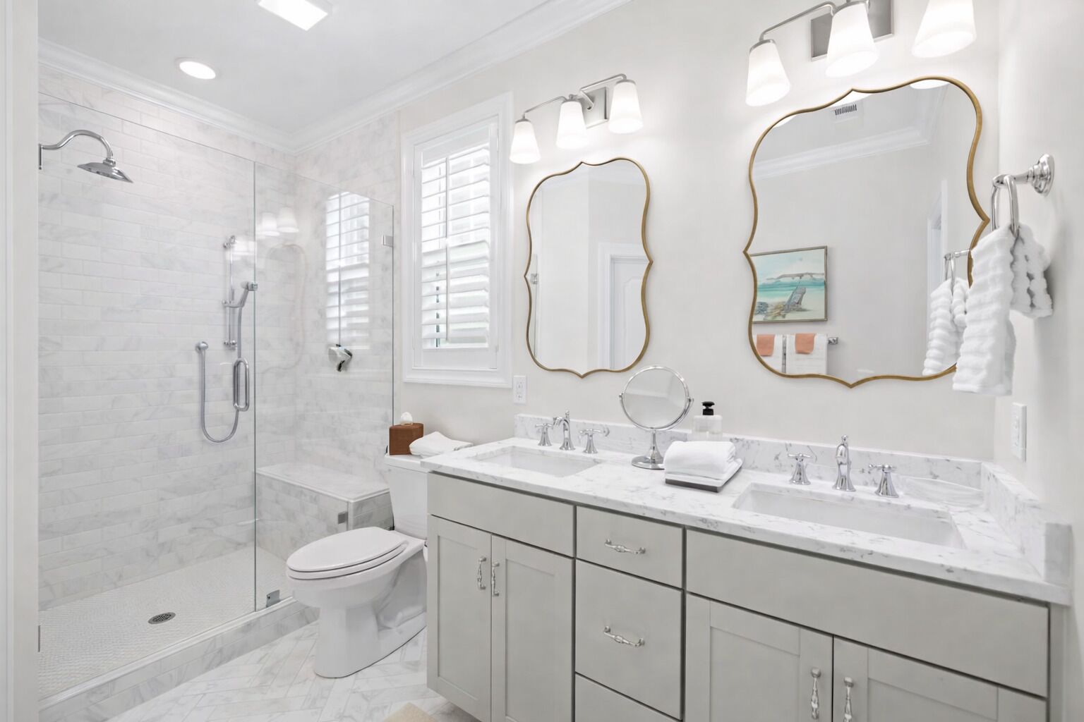 A modern bathroom with a glass-enclosed shower, a toilet, a vanity with two sinks, and a large mirror with a gold frame.
