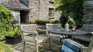 An outdoor patio with stone walls, wooden chairs, and a table set with wine glasses and a bottle. - Ty Fry Estate - sleeps 16 guests  in 8 bedrooms (Pentraeth/Red Wharf Bay)