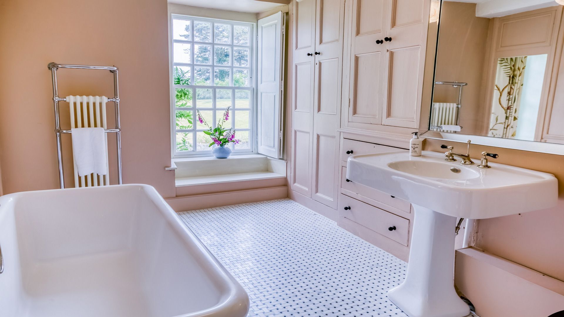 A bathroom with a bathtub, a sink, a window with a view of greenery, and a mirror.