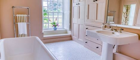 A bathroom with a bathtub, a sink, a window with a view of greenery, and a mirror.