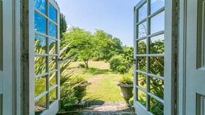 Una puerta abierta que da a un jardín cuidado, con un sendero despejado, rodeado de exuberante follaje y plantas florecientes.