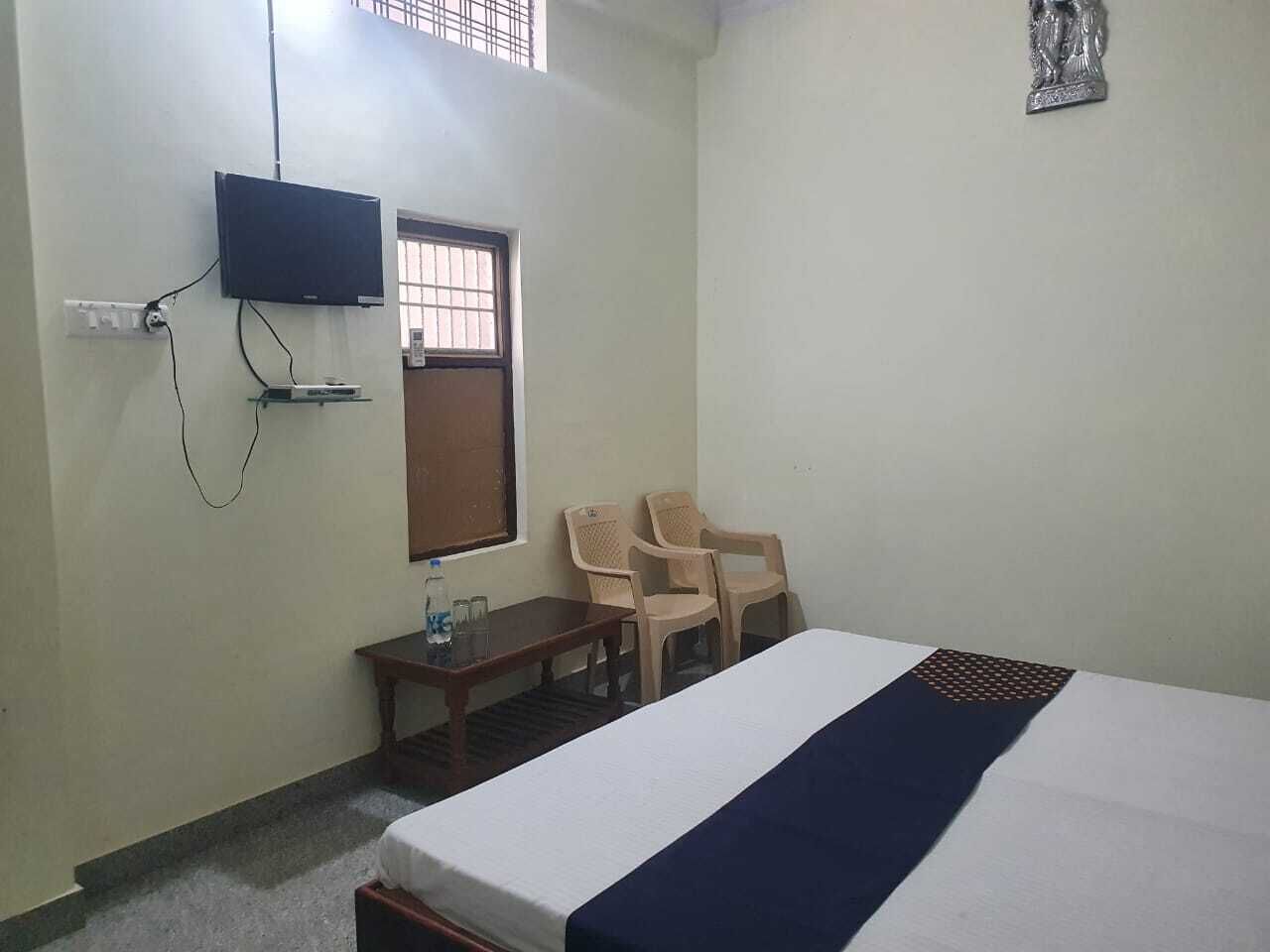 A hotel room with a bed, a TV mounted on the wall, a small table with chairs, and a window with bars.