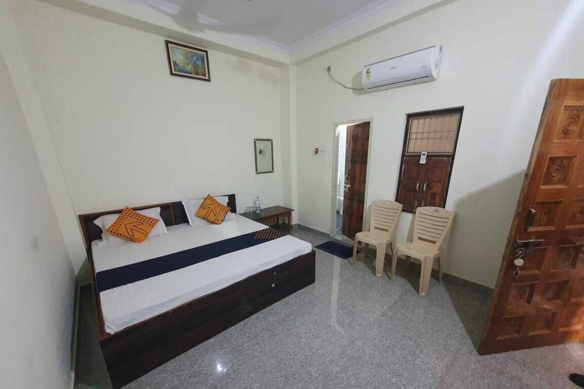 Un dormitorio con cama, escritorio, dos sillas, aire acondicionado y una puerta de madera.