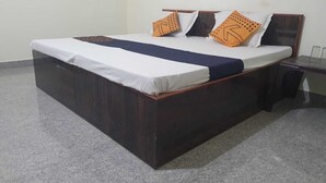 Una cama individual con estructura de madera oscura, ropa de cama blanca y dos almohadas naranjas con diseños negros.