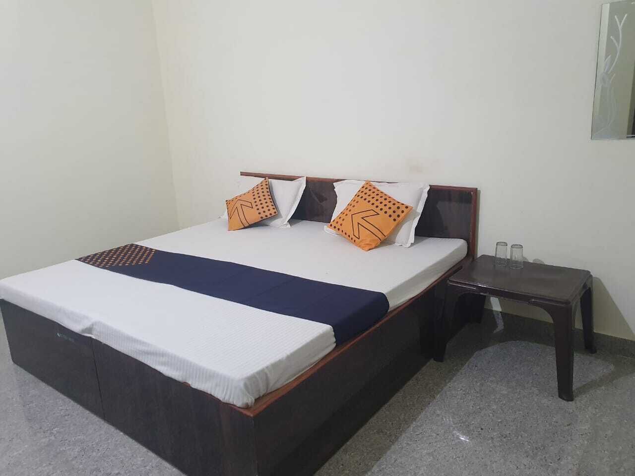 A single bed with a wooden frame, white bedding, and two orange pillows with a geometric pattern.